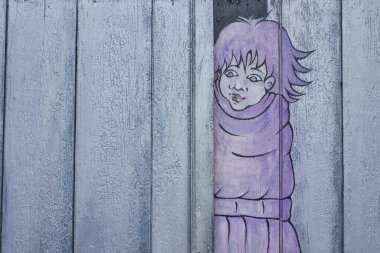 Pastel mor bir duvar resmi, geniş gözlü ve dikenli saçlı, eskimiş, açık mavi ahşap döşemeleri soyan, tuhaf ve kırsal bir etki yaratan bir çocuk figürü..