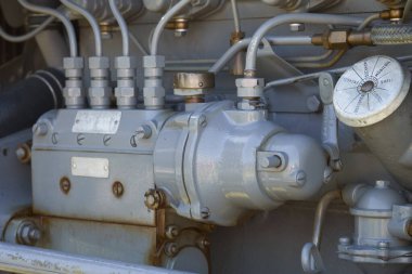 Eski, gri dizel motorun yakıt pompa sisteminin detaylı bir görüntüsü çeşitli hatlar, fındıklar ve karmaşık endüstriyel mekanikler gösteren bir 