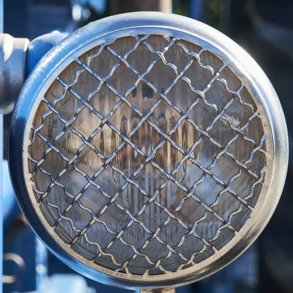 Dairesel, klasik endüstriyel bir farın yakın çekimi sağlam bir tel örgü koruyucusu tarafından korunuyor, dayanıklı tasarım ve metalik dokular sergiliyor..