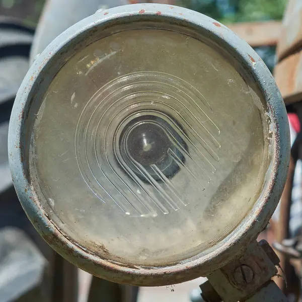 Eski bir traktörün kirli ve paslı eski bir farının yakın çekimi, yıpranmış cam mercek ve merkezi bir ampul gösteriyor, endüstriyel veya kırsal temalar için mükemmel..