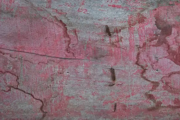 Yıpranmış kırmızı boyalı, yıpranmış kontrplak, görünür ahşap tanecikler, çatlaklar ve paslı zımbalar, engebeli ve dokulu bir arka plan oluşturuyor..