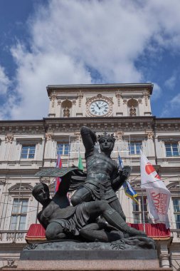 Bir Torino meydanında heybetli bronz bir binicilik heykeli, süslü bir saat kulesi ve mavi gökyüzünün altında tarihi İtalyan mimarisi..