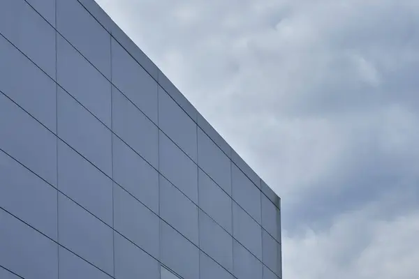 Mimari veya soyut tasarımlar için ideal, yumuşak, bulutlu bir gökyüzüne karşı kurulu, eğri, parlak mavi-gri bir bina cephesinin soyut görüntüsü.