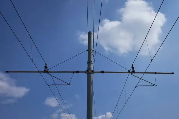 Kutuplar, kablolar ve izolatörlerin yer aldığı, beyaz bulutlu, modern altyapıyı temsil eden açık mavi gökyüzüne karşı inşa edilmiş bir demiryolu kateneri sisteminin yukarı bakış açısı..