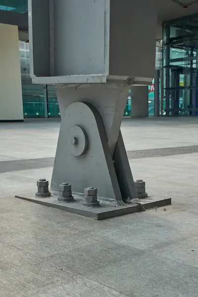 Açık gri beton zemin üzerinde sürgülü bağlantılar ve endüstriyel inşaat ayrıntıları içeren büyük bir çelik destek sütununun yakın çekimi.