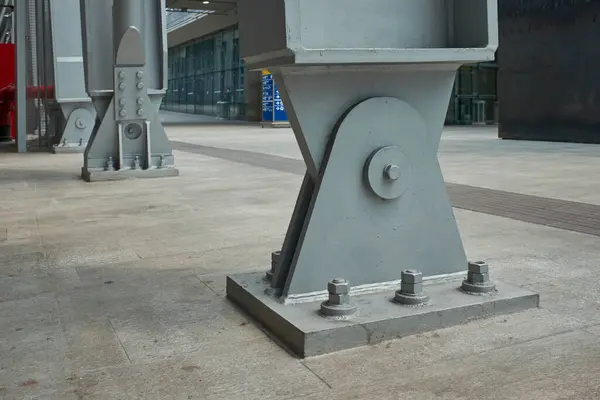 Sağlam çelik destek kirişine yakın çekim. Beton bir zemine demirlenmiş. Endüstriyel dayanıklılık ve modern yapı tasarımı sergiliyor..