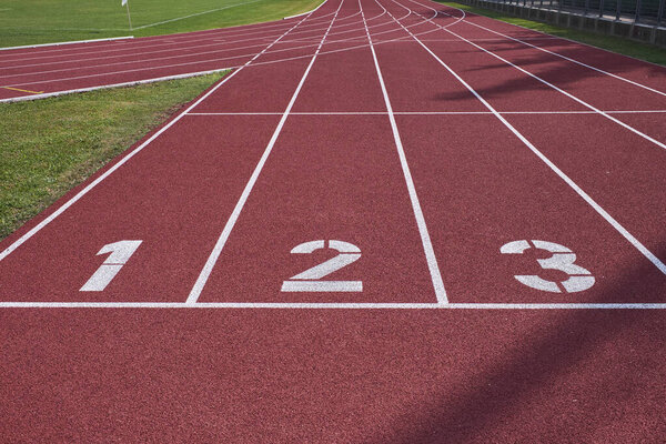 Широкий обзор полос 1-3 на красной легкоатлетической трассе, символизирующий соревнование, прогресс и начало гонки или фитнес-путешествия.