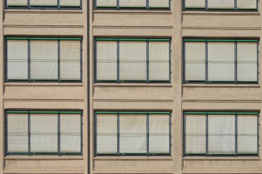 Tekrarlanan pencereleri ve kapalı perdeleri olan modern bir binanın simetrik cephesi. Kentsel mimari detay, tasarım, inşaat ve desenle ilgili konular için ideal.