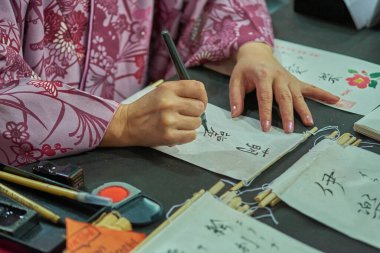 Geleneksel kimonolu bir kadının kültürel bir etkinlikte Japon kalemiyle mürekkep aletleri ve yazılı parşömenlerle çevrili bir şekilde çalışmasının yakın çekimi..