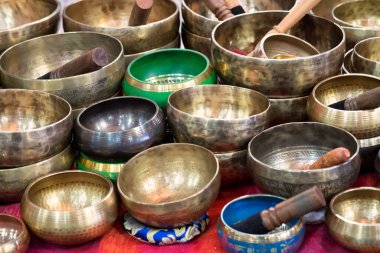 Meditasyon, ses terapisi ve ruhsal iyileştirme uygulamalarında kullanılan, pazarda sergilenen tahta sopalarla dolu renkli Tibet şarkı kaseleri koleksiyonu..