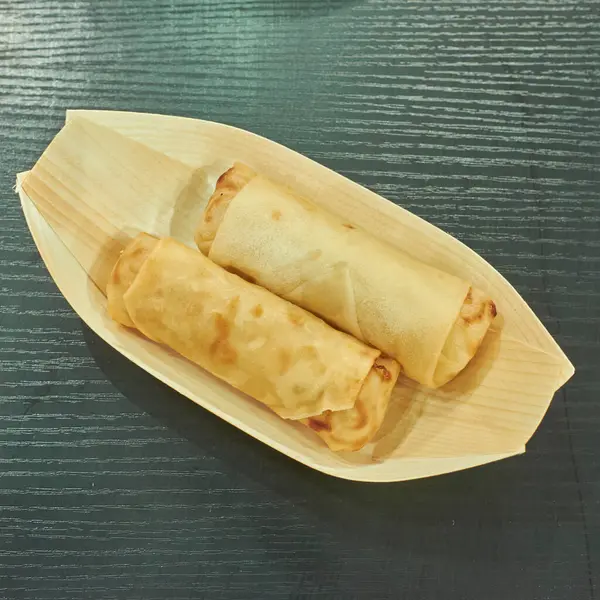 Çevre dostu bambu yaprağı tepsisinde sunulan iki altın çıtır börek, koyu ahşap bir masada sunuluyor. Klasik bir Asya sokak yemeği, yemek ve aperatif temaları için mükemmel..