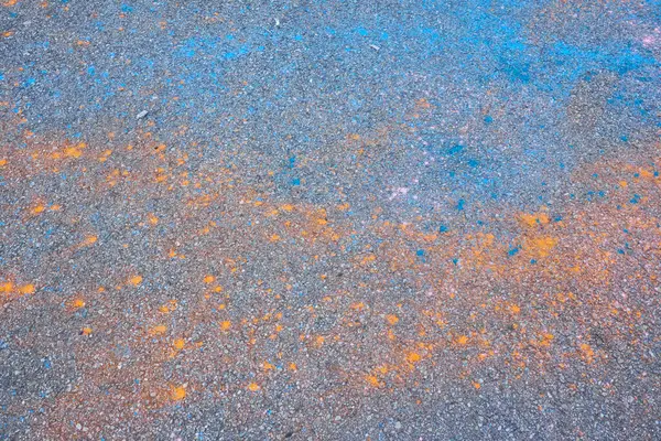 Holi 'den sonra asfalta serpilmiş canlı mavi, turuncu ve pembe toz. Kentsel ve şenlik dokusuna sahip canlı soyut bir arkaplan.