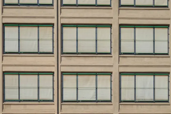 Tekrarlanan pencereleri ve kapalı perdeleri olan modern bir binanın simetrik cephesi. Kentsel mimari detay, tasarım, inşaat ve desenle ilgili konular için ideal.