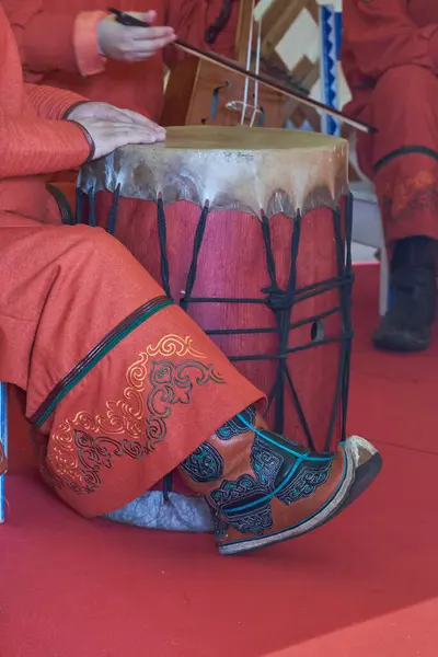 Canlı etnik kıyafetler ve çizmelerle geleneksel bir davul çalan Moğol müzisyenin yakın çekimi. Kültürel bir performans sırasında yakalanan, müzik, gelenek ve folklor temaları için ideal.