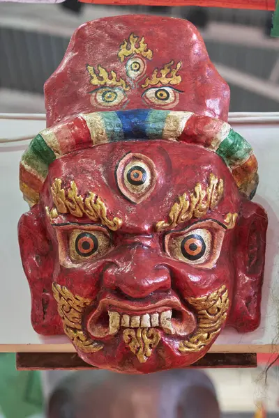 Vahşi bir ifade ve sembolik elementlerin yer aldığı canlı, el yapımı bir Tibet maskesinin yakın çekimi. Ayinlerde, törenlerde ya da geleneksel gösterilerde kullanılan bir kültür eseri..