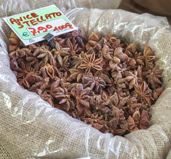 Fiyatla etiketlenmiş geleneksel bir pazarda çuval bezi içinde sergilenen yıldız anason baharatının yakın çekimi. Aşçılık, aromatik ya da tıbbi malzeme kullanımı için ideal.