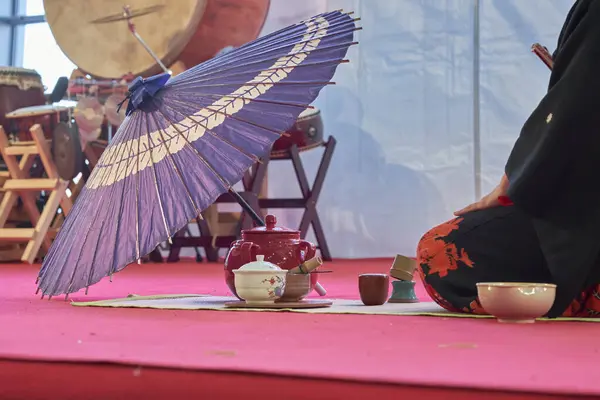 Japon çay seremonisi sahnesi çaydanlık, fincanlar, mor bir şemsiye, ve arka planda Taiko davulları, kapalı alandaki kültürel bir olay sırasında çekildi..