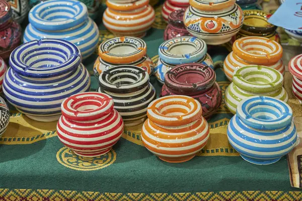 Çizgili ve dekoratif desenli parlak seramik kaplar geleneksel bir pazarda canlı bir tekstil üzerinde sergileniyor. Ev dekorasyonu veya zanaatkarlık için mükemmel..
