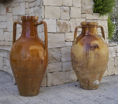 Geleneksel taş bir duvarın önünde yan yana duran iki kırsal terracotta kavanozu Güney İtalyan cazibesini çağrıştırıyor..