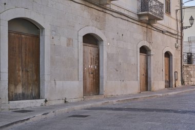 Yıpranmış kireçtaşı cephesi taştan kemerlerin altındaki ahşap kırsal kapılar. Sessiz kaldırım taşlı sokakta klasik Akdeniz mimarisi.