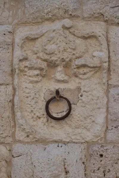 Yıpranmış kireçtaşı yardım heykeli. Metal yüzük takılı oyulmuş insan yüzü. Ortaçağ işçiliği sergileniyor.