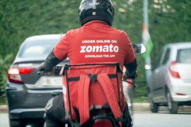 Delhi, Hindistan - takriben 2022: Hindistandaki gıda teknolojisi uygulaması ve ikonik kırmızı üniformalı Hindistan 'daki Zomato markalı sıcak kutulu bisikletçi teslimatçı çocuk.