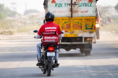 Delhi, Hindistan - takriben 2022: Hindistandaki gıda teknolojisi uygulaması ve ikonik kırmızı üniformalı Hindistan 'daki Zomato markalı sıcak kutulu bisikletçi teslimatçı çocuk.