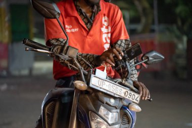 Delhi, Hindistan - 2022 dolaylarında: Zomato bisikletli bisikletçi Delhi Hindistan 'daki gıda teknolojisi girişiminin büyümesini gösteren ikonik kırmızı üniformayla cadde tarafında siparişi almak için bekliyor