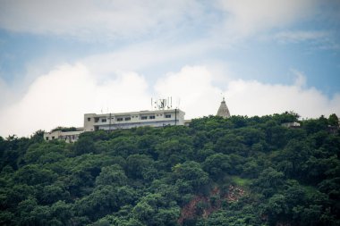 Jaipur 'da aravalli tepesinde tapınak kulesi olan beton bina yeşil ağaçlarla çevrili beyaz muson bulutlarına karşı.