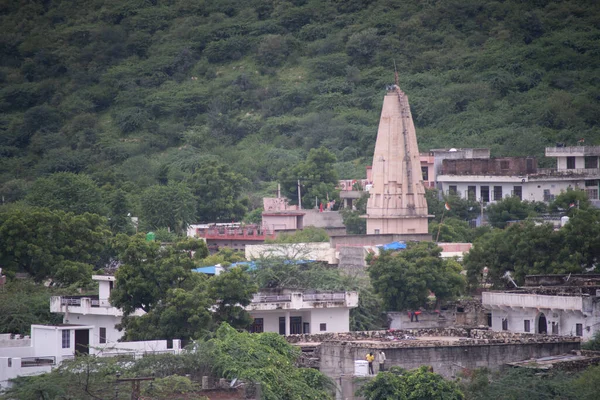 寺院の塔はジャイプールインドの距離に緑の丘と小さなコンクリートの家の真ん中に上昇尖塔 — ストック写真
