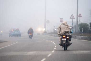 Delhi, Hindistan - 2023 dolaylarında: soğuk kış sabahı yoğun siste Hindistan 'dan daha az trafiği olan şallarla kaplı motosikletli adamlar