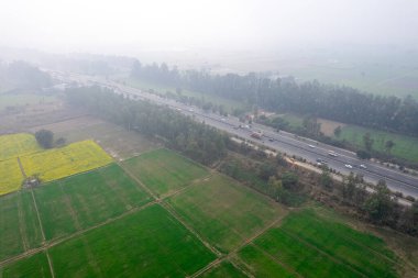aerial drone shot flying over yellow and green mustard feilds towards busy large highway lost in fog near rajasthan punjab in India Asia