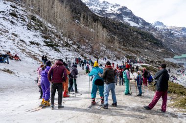 Kullu, India - circa 2022: Panning shot of crowd of people in winter wear playing in snow, sking, sliding, at snow point in lahul, manali solang a popular tourist spot during winters