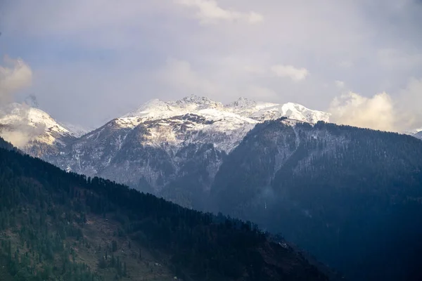 stock image fog mist rolling over tree covered mountains in the foreground and snow capped peak in the background in manali himachal pradesh In India