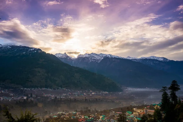 stock image monsoon clouds moving over snow covered himalaya mountains with the blue orange sunset sunrise light with town of kullu manali valley at the base of mountains India