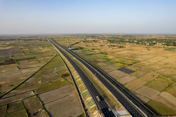 stock image locked tripod aerial drone shot of new delhi mumbai jaipur express elevated highway showing six lane road with green feilds with rectangular farms on the sides