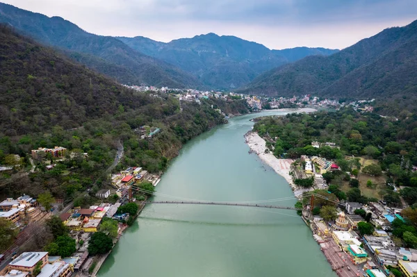 stock image aerial drone shot of blue water of river ganga stretching into distance with himalayas with ram setu suspension bridge and temples on the banks of the river