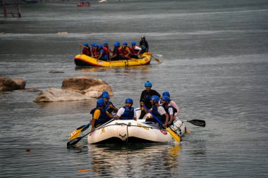Rishikesh, Haridwar, Hindistan - 2023 dolaylarında kask ceketli insanlar yaz aylarında Shivpuri 'den Rishikesh' e rafting yaptıktan sonra salda kıyıya kürek çekiyorlar.
