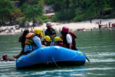 Rishikesh, Haridwar, Hindistan - 2023 dolaylarında aile dostları salda oturmuş Ganga nehrinin kıyısındaki ghat ve tapınağın önünden geçerken macera sporlarının tadını çıkarıyorlardı.