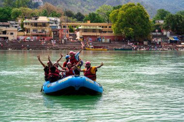Rishikesh, Haridwar, Hindistan - takriben 2023: İnsanlar helyumlar ve can yelekleriyle beyaz su nehrinin keyfini çıkararak Ganga 'nın serin yeşil sularında rafting yapıyorlar popüler bir yaz sporu.