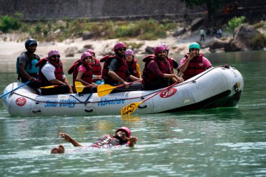 Rishikesh, Haridwar, Hindistan - 2023 dolaylarında: Bir grup insan, arkadaş, aile şişme bir salın yanında mavi yeşil Ganga sularında yüzüyor ve popüler bir macera sporu içine çekiliyor.