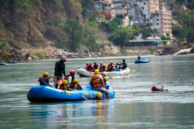 Rishikesh, Haridwar, Hindistan - 2023 dolaylarında: Bir grup insan, arkadaş, aile şişme bir salın yanında mavi yeşil Ganga sularında yüzüyor ve popüler bir macera sporu içine çekiliyor.