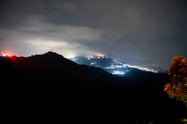 Hindistan 'da turuncu ve mavi ışıklarla dolu Darjeeling köyünü gösteren bir gece fotoğrafı.