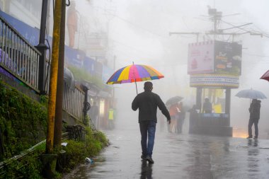 Darjeeling West Bengal 'in sisli sokakları boyunca renkli şemsiyeler taşıyan adam kasabanın doğal güzelliğini gösteriyor.