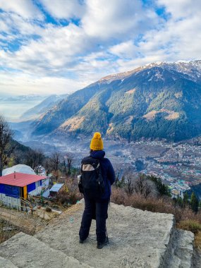 Dişi yürüyüşçü köydeki evlere ve Himalaya dağlarına uzaktan bakıyor ve Hindistan 'da manali, kullu, shimla, kedarnath' da bulutlu gökyüzüne.