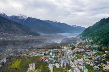 Hava aracı görüntüsü vadideki manali kullu kasabayı sisle kaplı himalaya dağları ve Hindistan 'daki tepe istasyonlarının güzelliğini gösteren yeşil alanlar arasında gösteriyor.