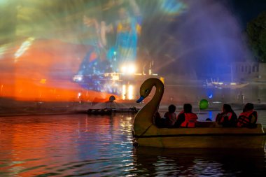 People in a swan shaped boat enjoying the light, sound and fountains show at Gadisar lake showing the famous tourist spot near Jodhpur and a place to relax in India clipart