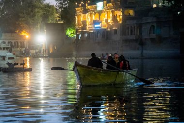 Family enjoying a night boat ride on the lit waters of Gadisar lake in Jaisalmer Jodhpur with the scenic palace and domes nearby a popular tourist destination India clipart