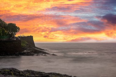 Tourists enjoying the view at Sinquerim Aguada fort with high monsoon waves at dusk splashing against the huge stone walls of the tower in goa Maharashtra India clipart