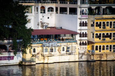 Geleneksel taş binalar, Udaipur 'daki Pichola Fateh Efsanesi' nin kıyısında su yollarında tekneleri olan restoranlar.